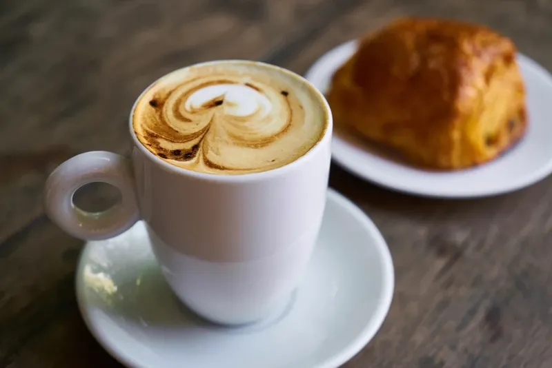 A cappuccino and a croissant on a wooden table