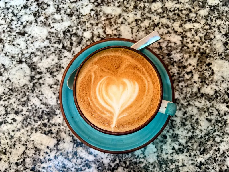 A latte with heart-shaped foam art in a teal cup