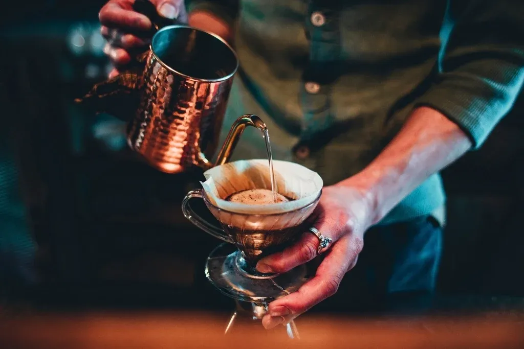 A barista pouring hot water over a pour-over coffee filter